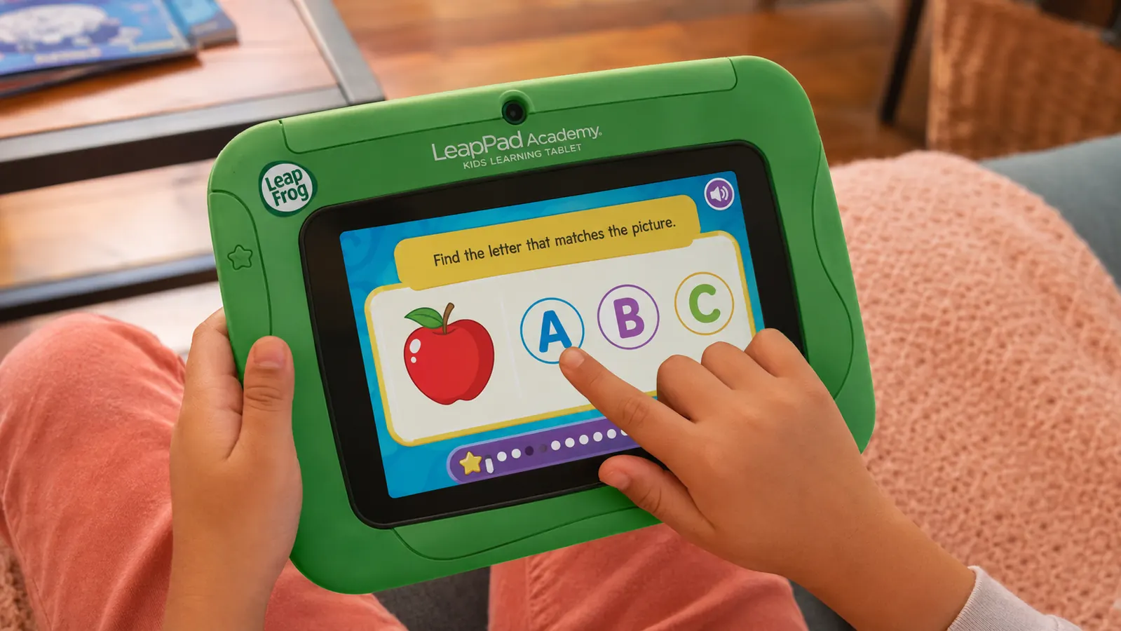 Close-up of a child's hands pressing the screen of a LeapFrog LeapPad Academy learning tablet showing a colorful alphabet activity